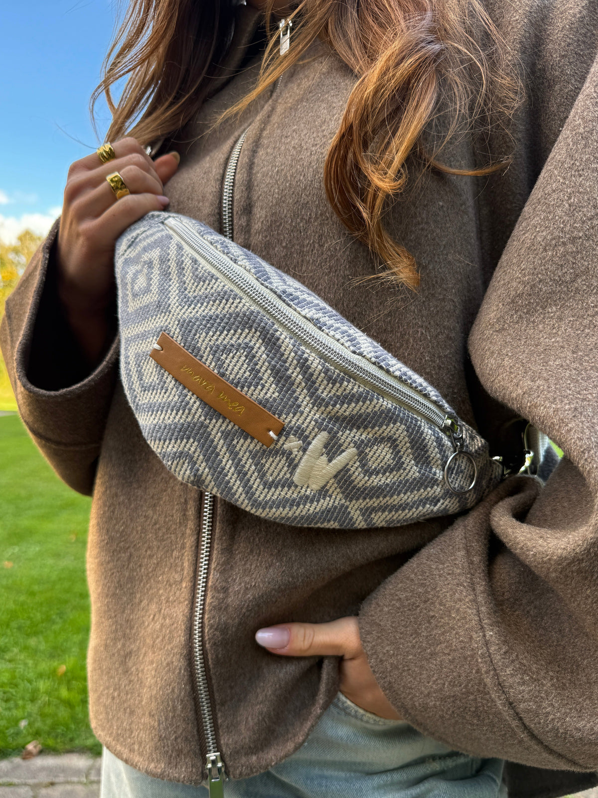 Nahaufnahme der Mini Bauchtasche mini me vor dem Körper, Rautenmuster mit braunem Logo-Etikett