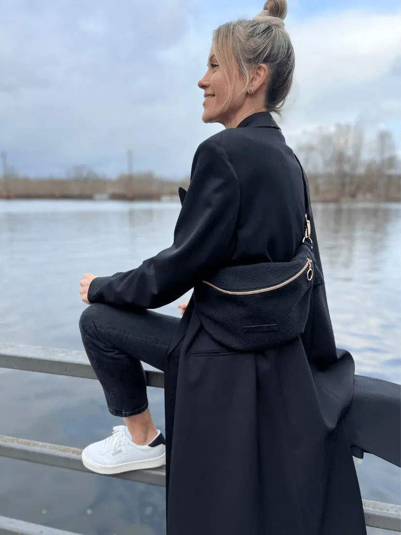 Schwarze gesteppte Crossbody Tasche mit breitem Gurt und goldenen Details, getragen auf der Seite in der Stadt am See.