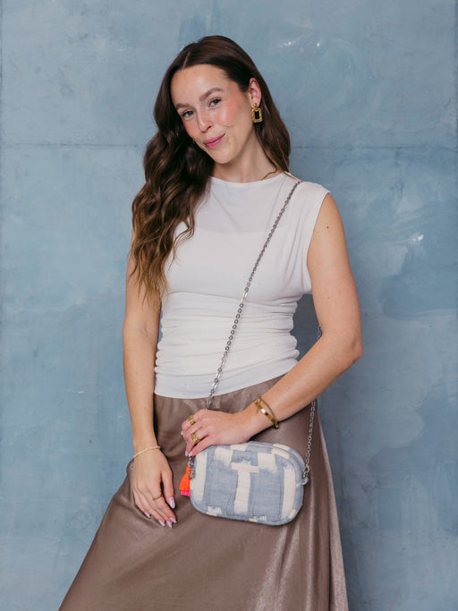 Frau trägt die mara mea Umhängetasche air kiss in Hellblau-Offwhite mit silberfarbener Kette und neon-orange-pinker Quaste