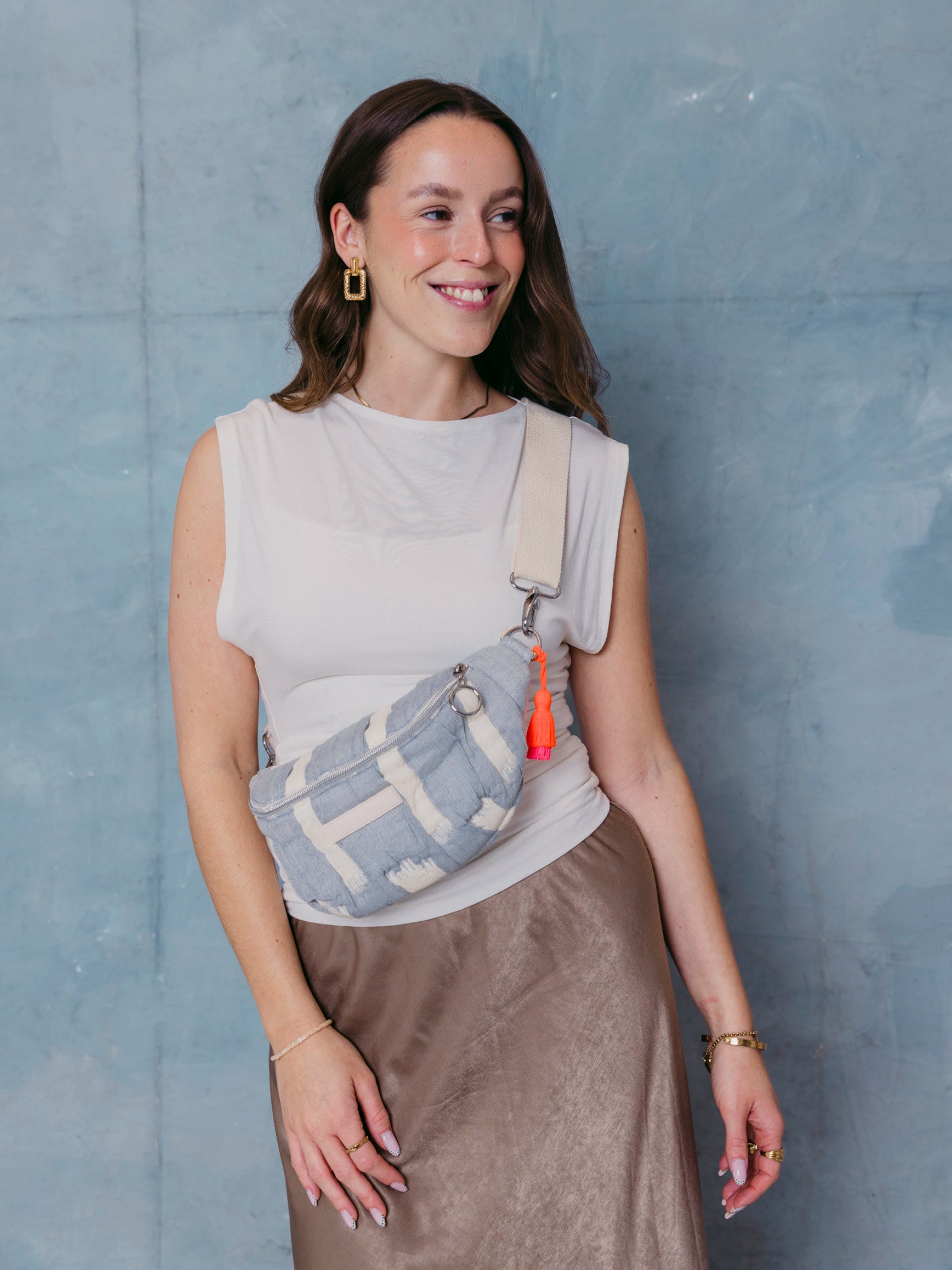 Frau trägt die mara mea Mini Bauchtasche cloud club in Hellblau-Offwhite mit breitem  verstellbarem Schultergurt, silbernem Ring-Zipper und neon-orange-pinker Quaste