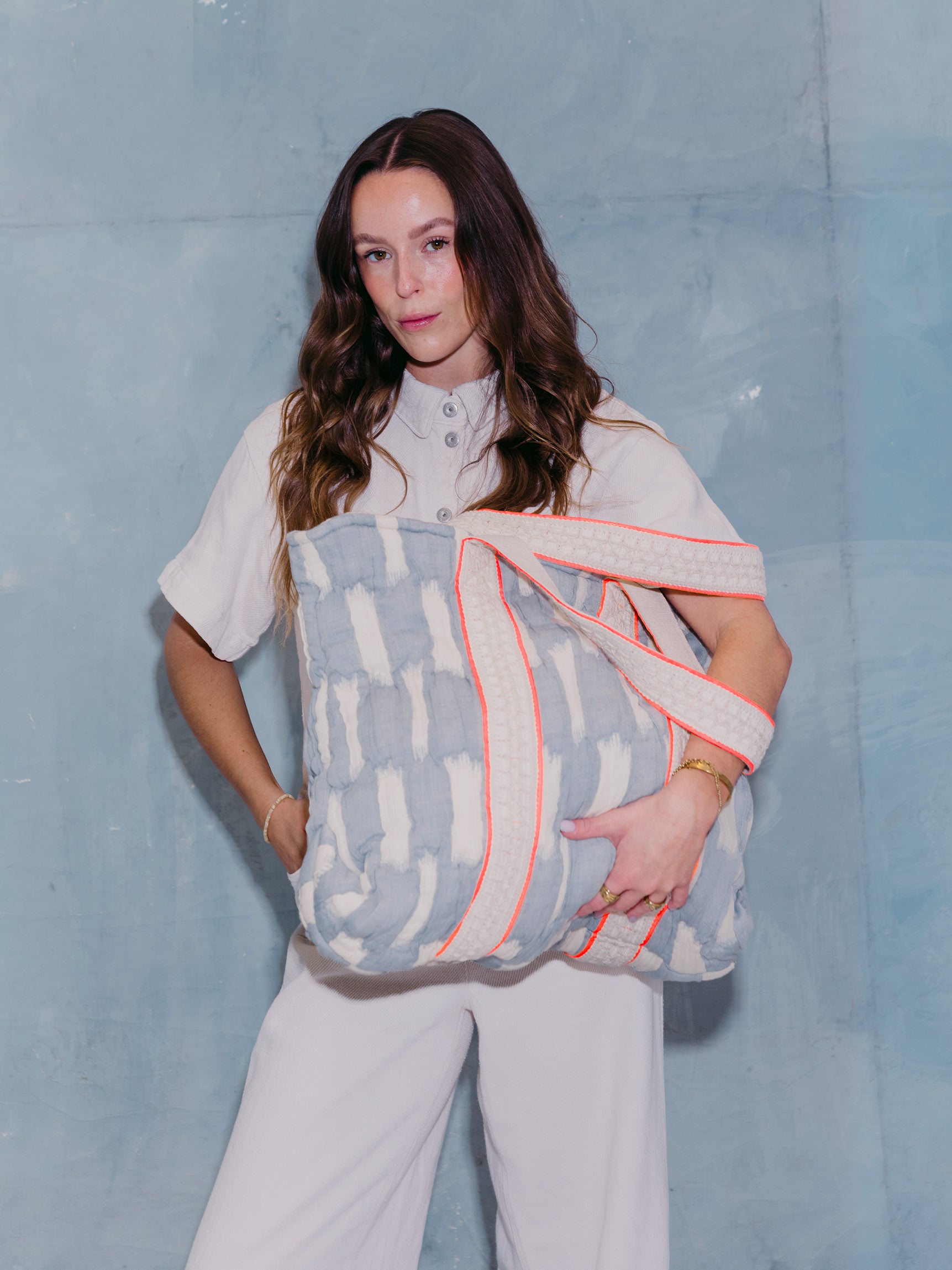 Frau hält die mara mea Shopper Bag sky state in Hellblau-Offwhite mit breiten gewebten Baumwollgriffen und neon-oranger Paspel vor dem Körper