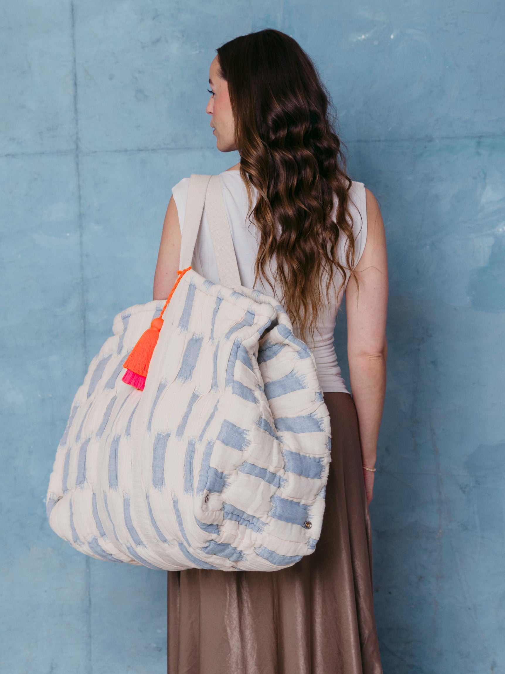 Frau trägt die extra große mara mea Schultertasche in Hellblau-Offwhite mit Baumwollgriffen und neon-orange-pinker Quaste über der Schulter