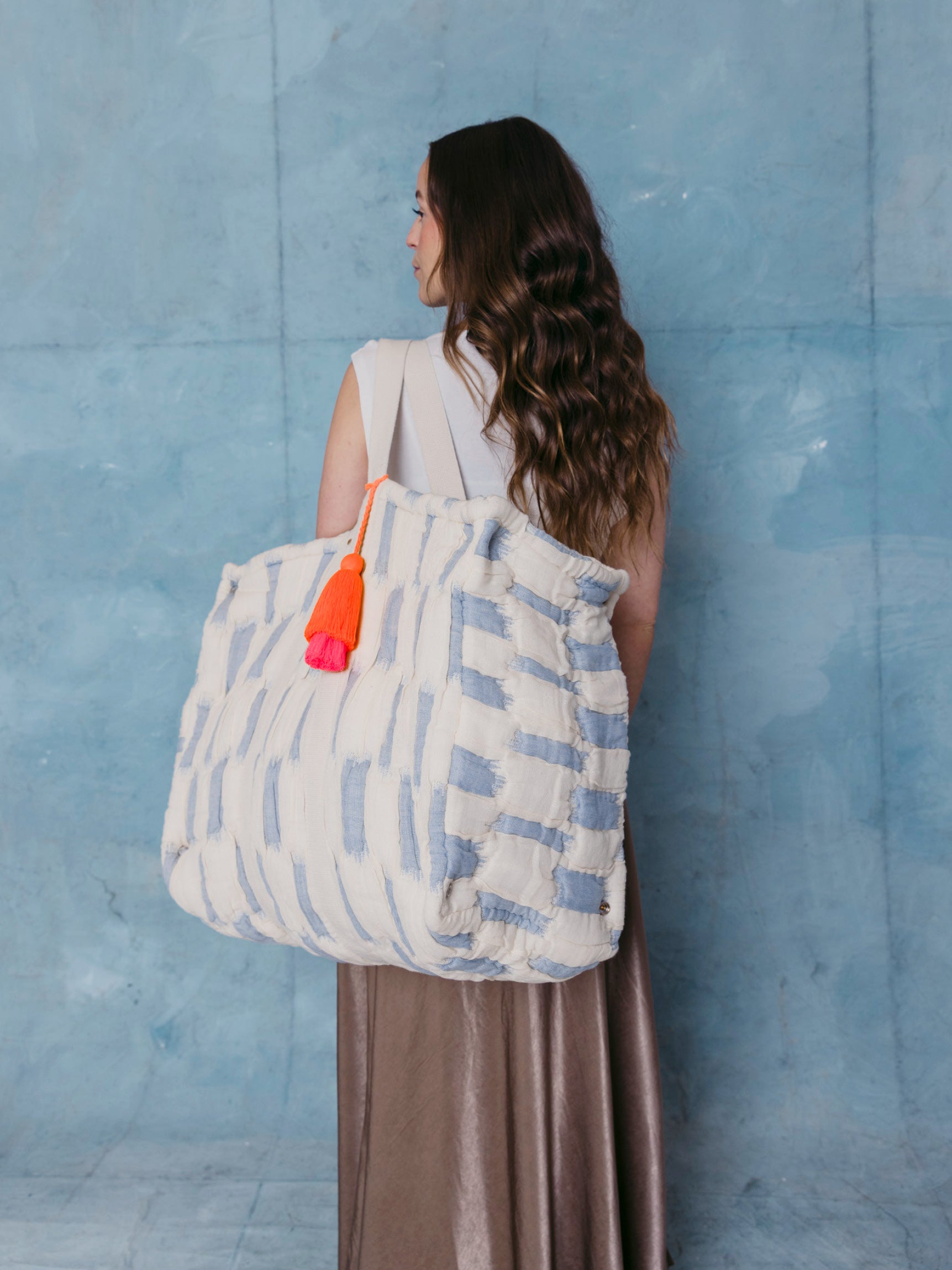 Frau trägt die extra große mara mea Schultertasche in Hellblau-Offwhite mit neon-oranger Quaste über der Schulter