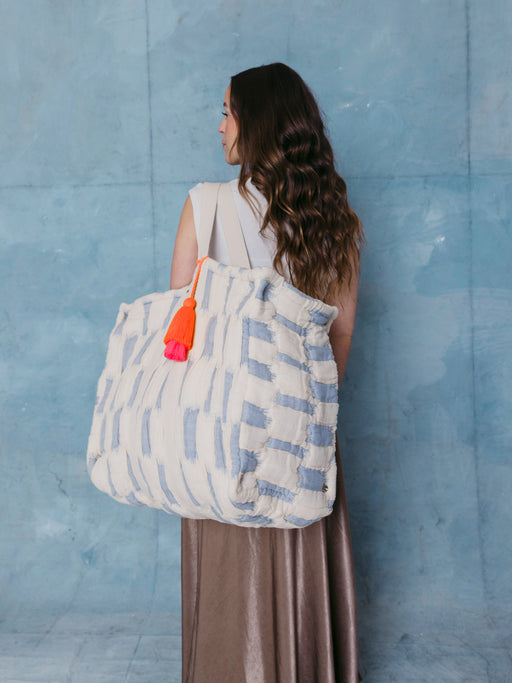 Frau trägt die extra große mara mea Schultertasche in Hellblau-Offwhite mit neon-oranger Quaste über der Schulter