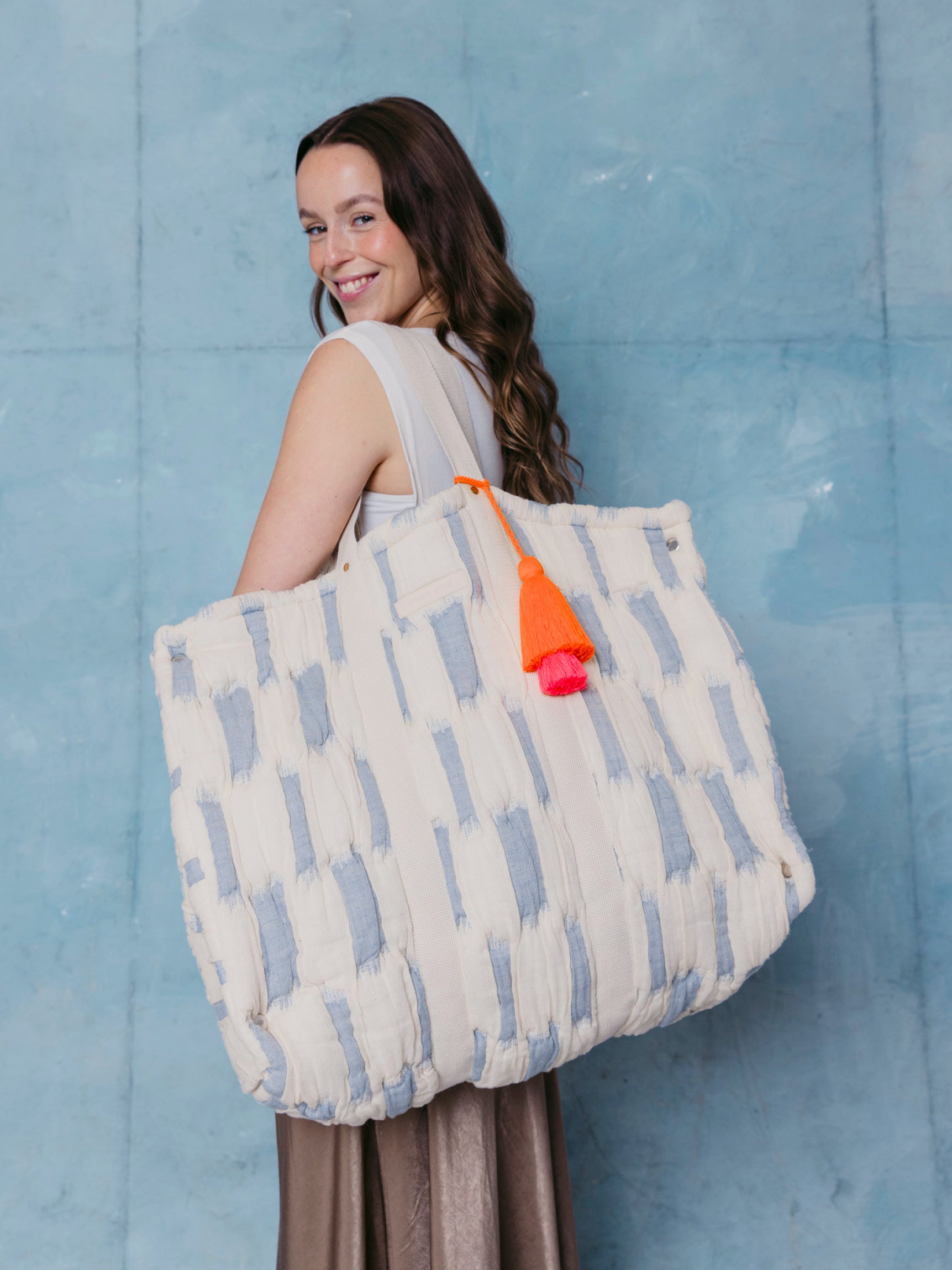 Frau trägt die extra große mara mea Schultertasche in Hellblau-Offwhite mit Baumwollgriffen und neon-oranger Quaste über der Schulter