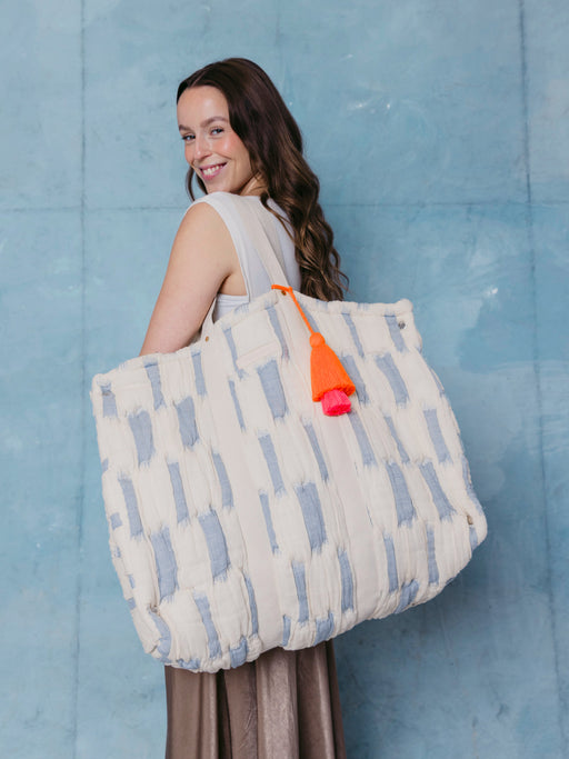 Frau trägt die extra große mara mea Schultertasche in Hellblau-Offwhite mit Baumwollgriffen und neon-oranger Quaste über der Schulter