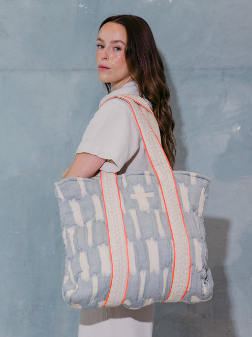 Frau trägt die mara mea Shopper Bag sky state in Hellblau-Offwhite mit breiten gewebten Baumwollgriffen und neon-oranger Paspel über der Schulter