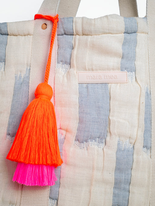 Detailansicht der extra großen mara mea Schultertasche in Hellblau-Offwhite mit Markenlabel, Baumwollgriff und neon-orange-pinker Quaste
