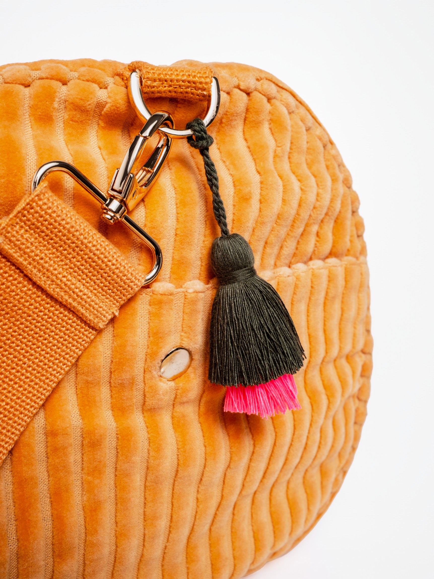 Detailansicht der orangefarbenen mara mea Weekender-Tasche True Colors Peach aus Cord mit Gurtkarabiner, Metallring und schwarz-pinkem Quastenanhänger