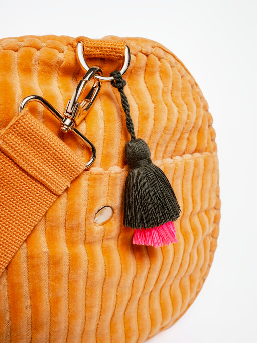 Detailansicht der orangefarbenen mara mea Weekender-Tasche True Colors Peach aus Cord mit Gurtkarabiner, Metallring und schwarz-pinkem Quastenanhänger