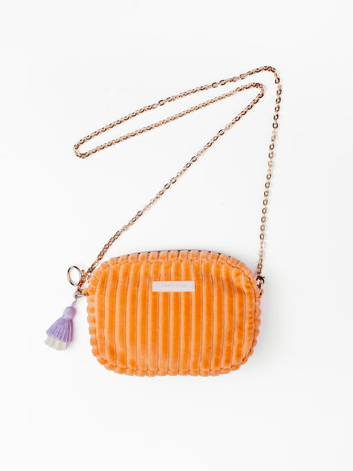 Orangefarbene mara mea Umhängetasche Peach Please Peach aus Cord mit goldfarbener Kette und lilafarbenem Quastenanhänger auf weißem Hintergrund