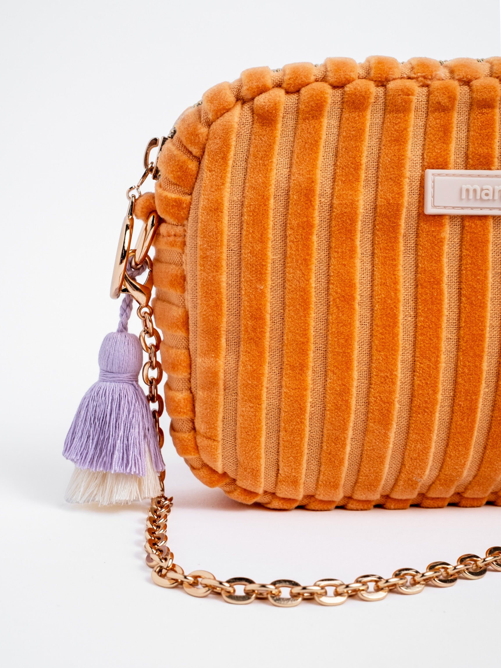 Detailansicht der orangefarbenen mara mea Umhängetasche Peach Please Peach aus Cord mit goldfarbener Kette und lilafarbenem Quastenanhänger