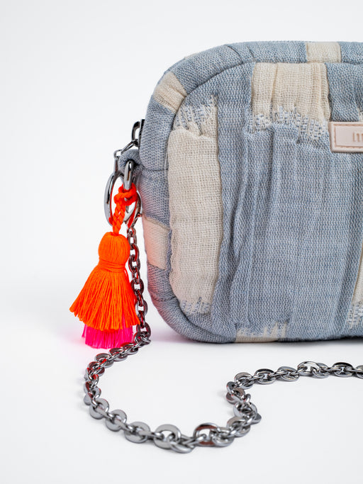 Detailansicht der mara mea Umhängetasche air kiss in Hellblau-Offwhite mit silberfarbener Kette, silbernem Metallring-Reißverschluss und neon-orange-pinker Quaste