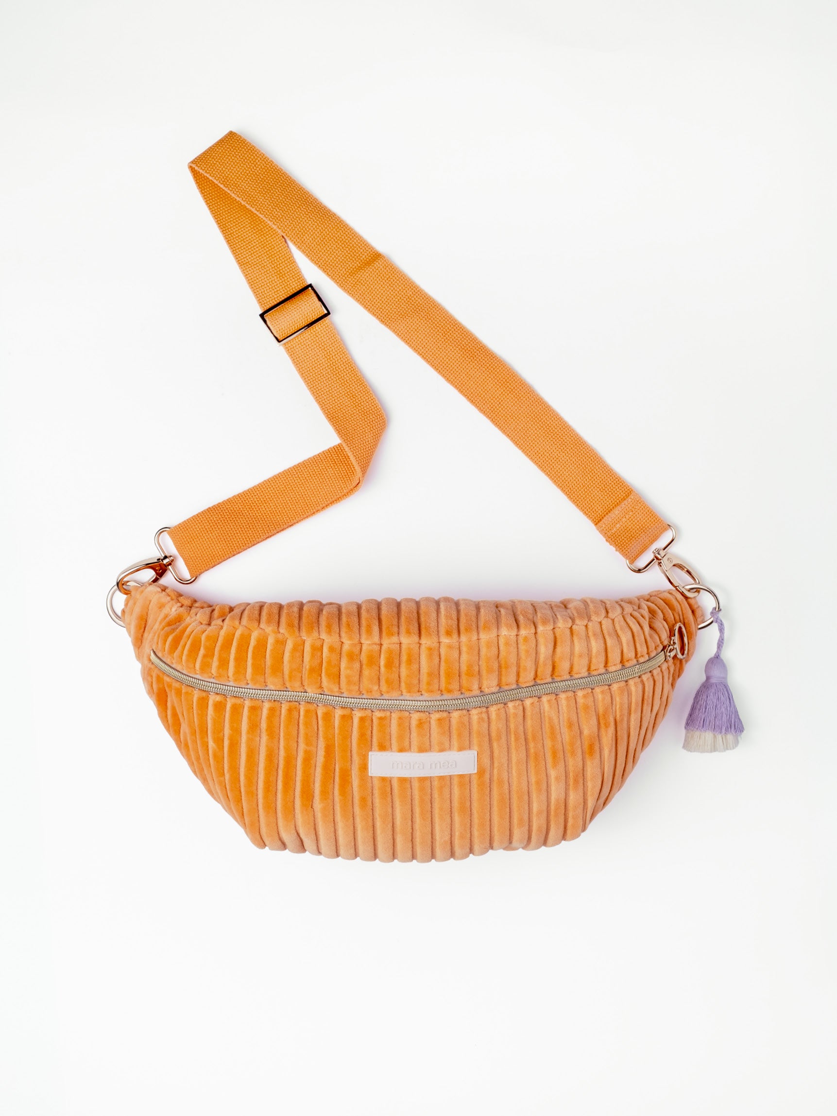Orangefarbene mara mea Maxi Bauchtasche Soft Serve Peach aus Cord mit verstellbarem Gurt, Reißverschluss und lilafarbenem Quastenanhänger auf weißem Hintergrund