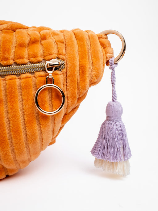 Detailansicht der orangefarbenen mara mea Maxi Bauchtasche Soft Serve Peach aus Cord mit Reißverschluss, Metallring und lilafarbenem Quastenanhänger