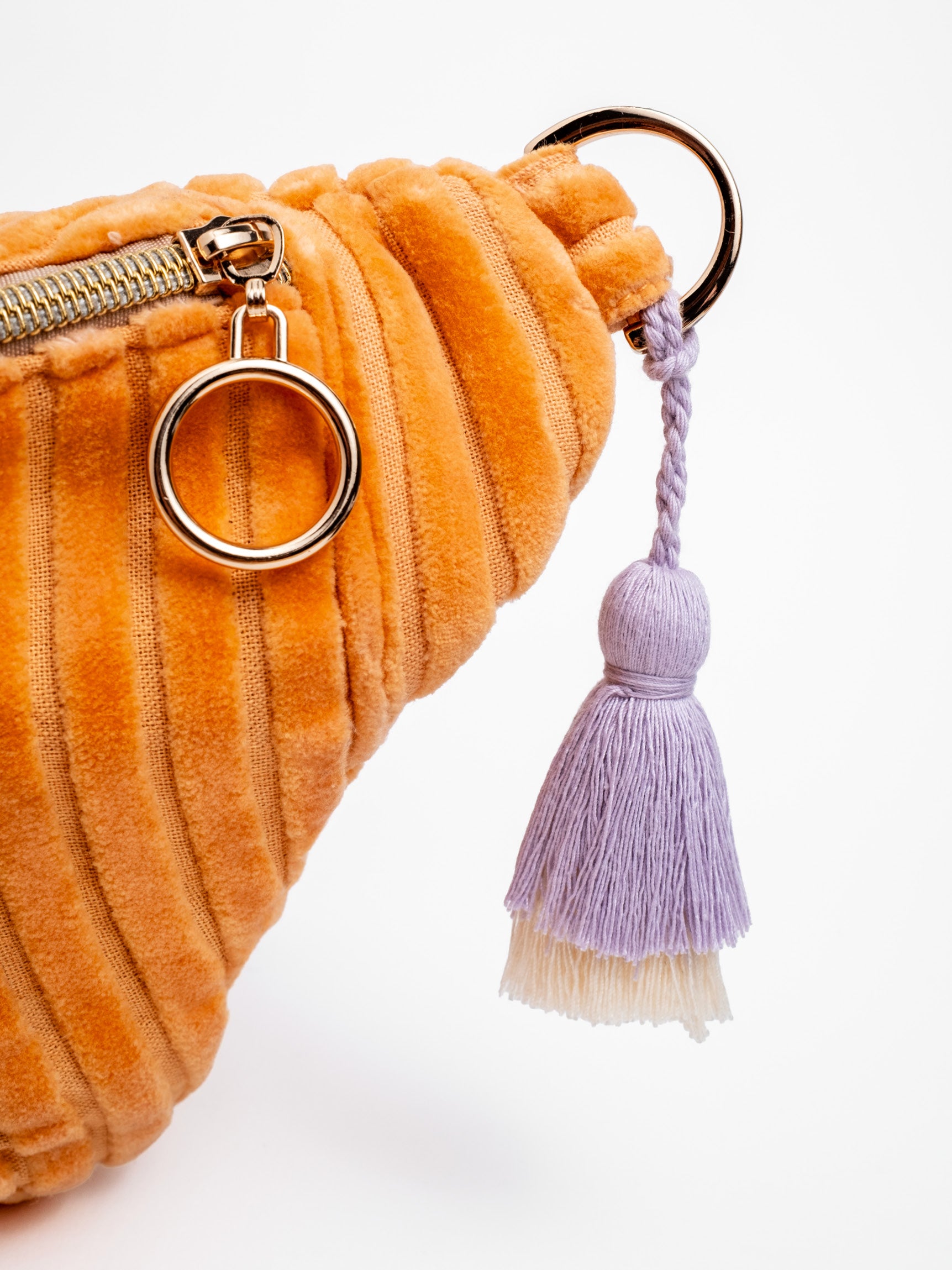 Detailansicht der orangefarbenen mara mea Midi Bauchtasche Sunset Date Peach aus Cord mit Reißverschluss, Metallring und lilafarbenem Quastenanhänger