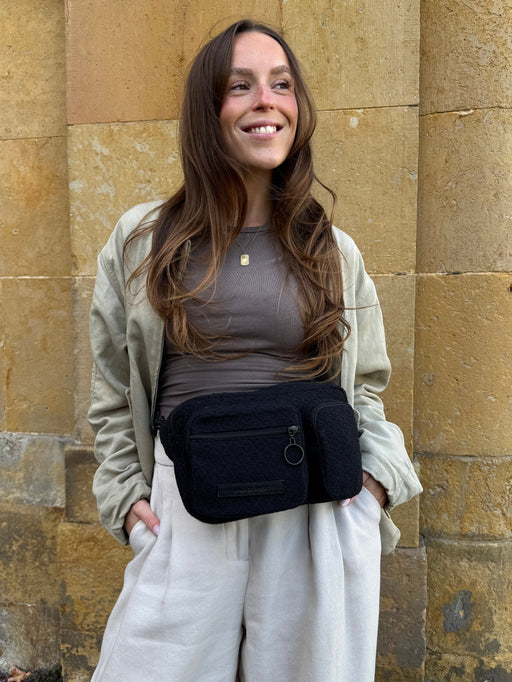 Frau trägt die schwarze Hip Bag all black um die Hüfte zu heller Jacke und weißer Hose
