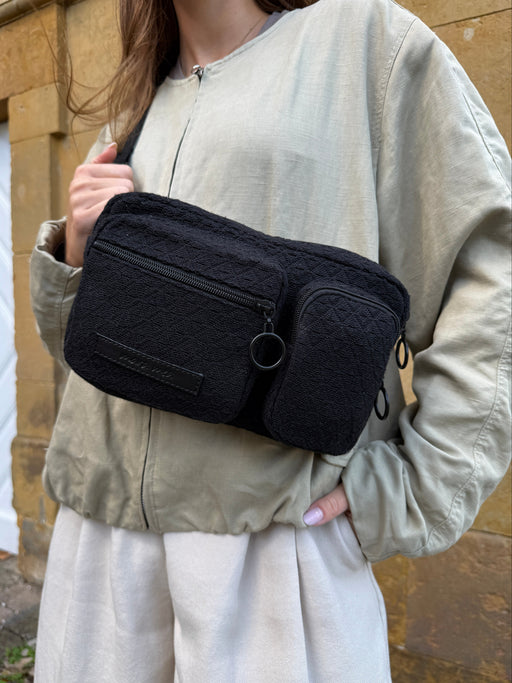 Hip Bag all black crossbody getragen, Nahaufnahme der beiden Reißverschlussfächer mit schwarzen Ringen