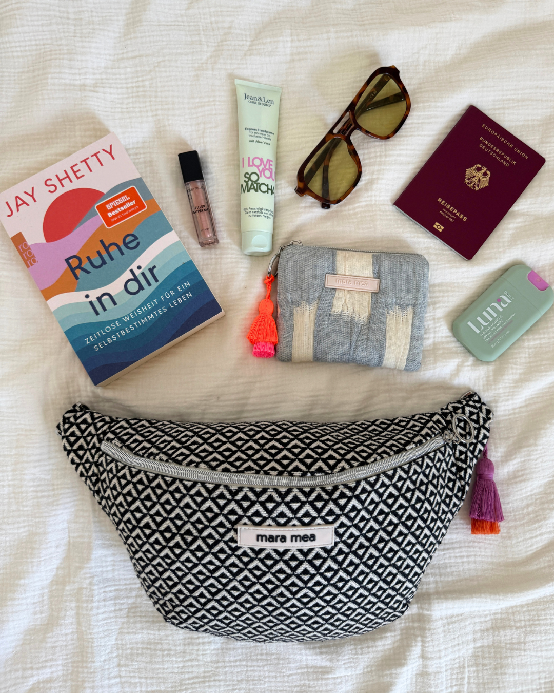 Bauchtasche catching up neben Buch, Sonnenbrille, Reisepass und Portemonnaie