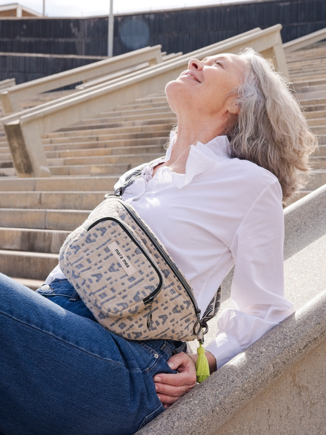 Älteres Modell sitzt halb liegend auf Treppe gestützt in der Sonne und trägt dabei die Midi Bum Bag win me over.