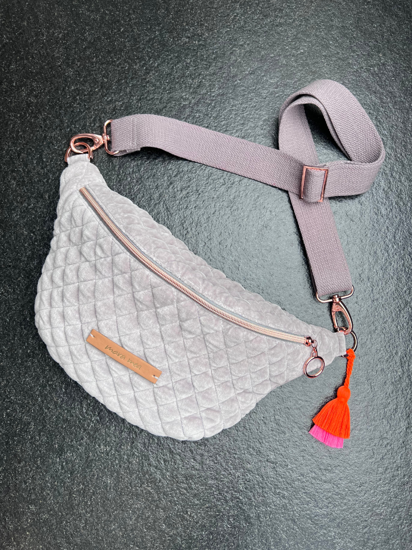 Produktaufnahme von oben der grauen Midi-Bumbag aus abgestepptem Samt. Tessel aus Neonorange und Pink. Rosegoldener Reißverschluss.