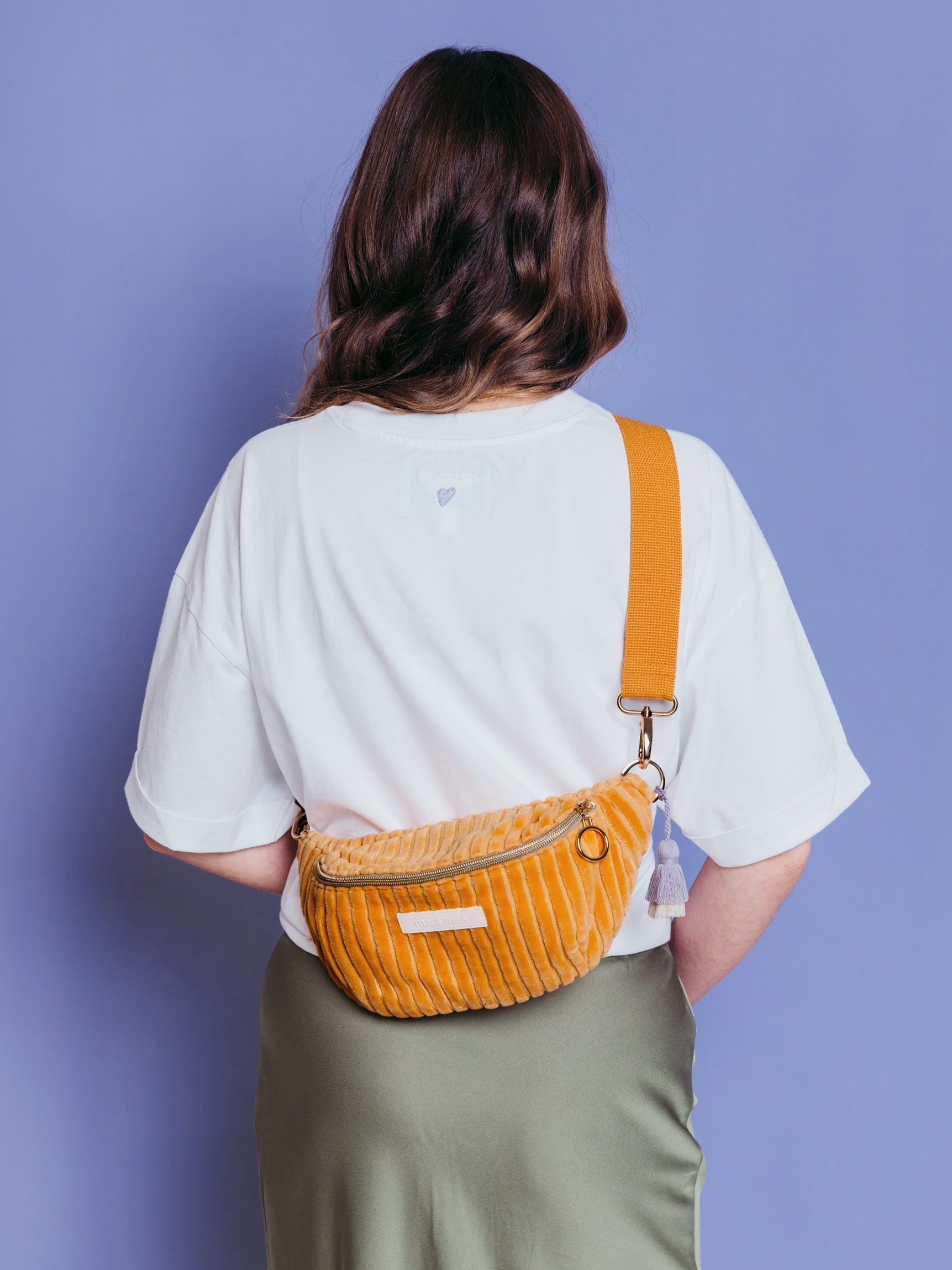 Frau trägt die orangefarbene mara mea Mini Bauchtasche Come Dancing Peach aus Cord quer über dem Rücken vor blauem Hintergrund
