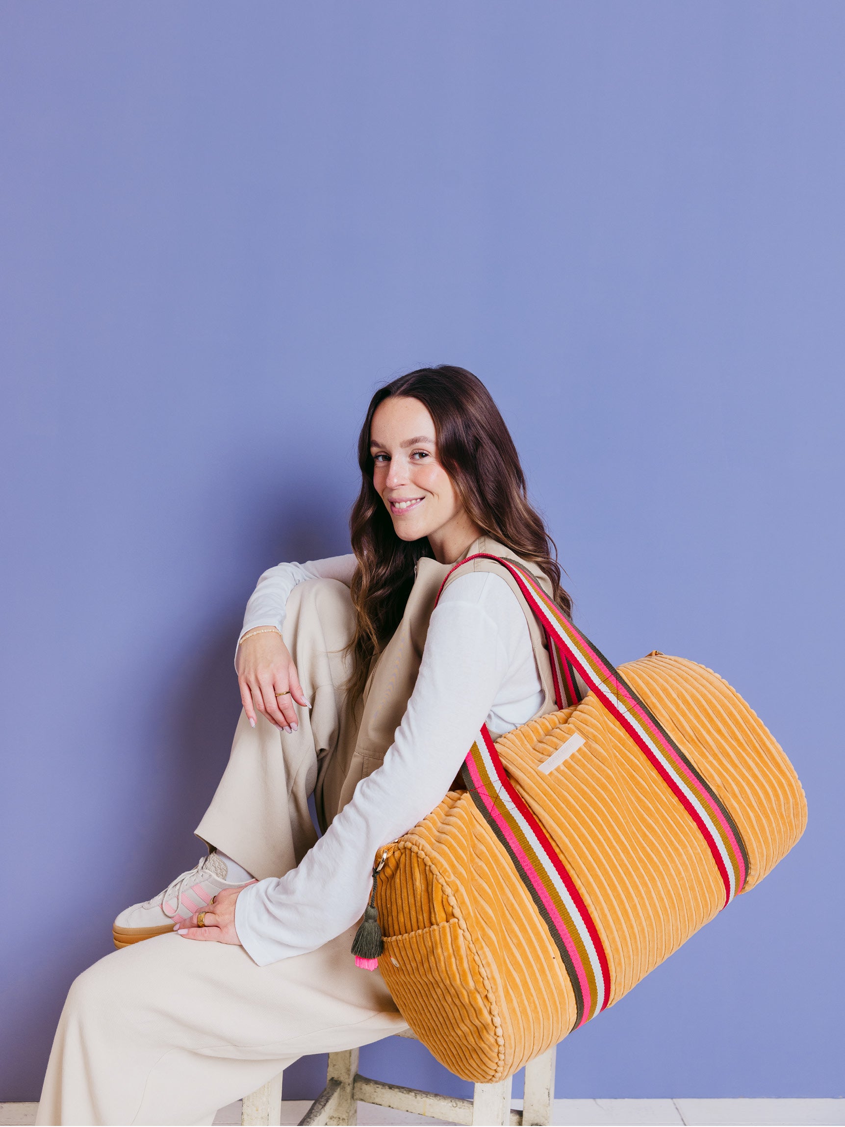 Sitzende Frau trägt die orangefarbene mara mea Weekender-Tasche True Colors Peach aus Cord an bunten Tragegriffen vor blauem Hintergrund