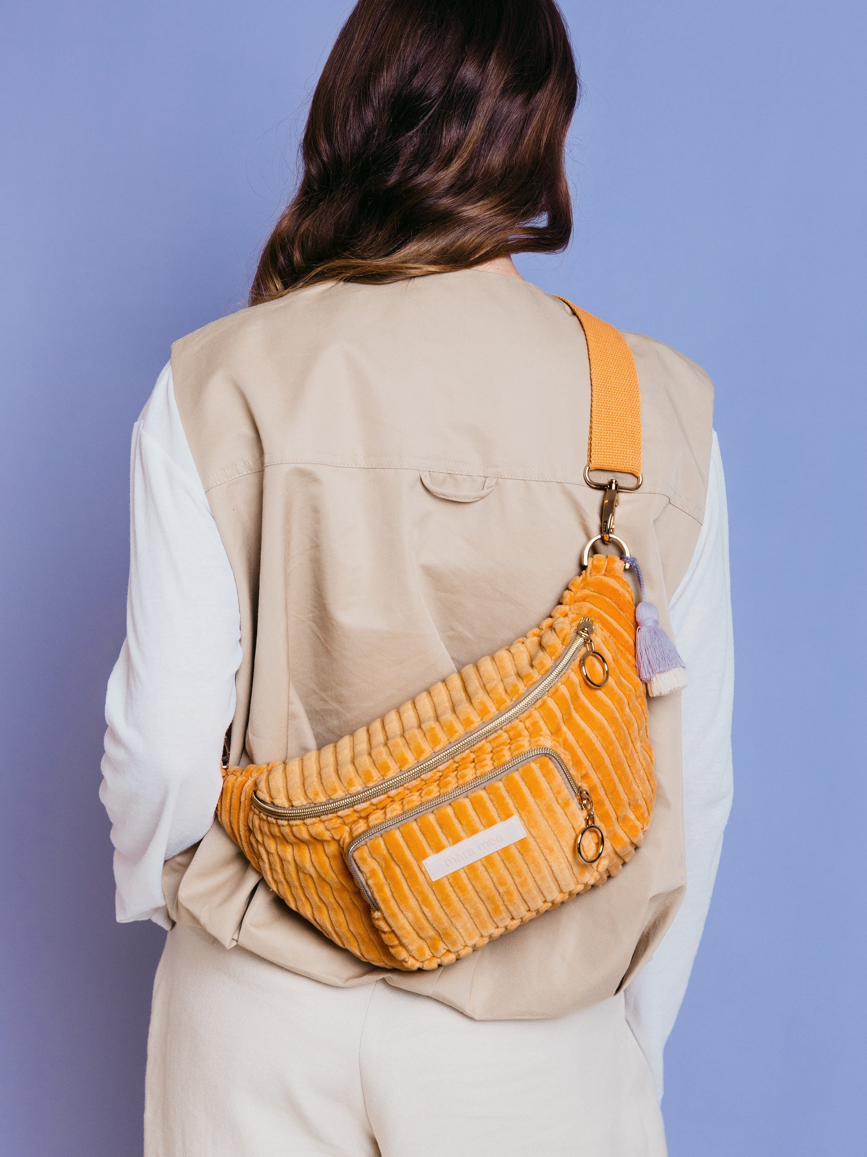 Frau trägt die orangefarbene mara mea Midi Bauchtasche Sunset Date Peach aus Cord quer über dem Rücken vor blauem Hintergrund
