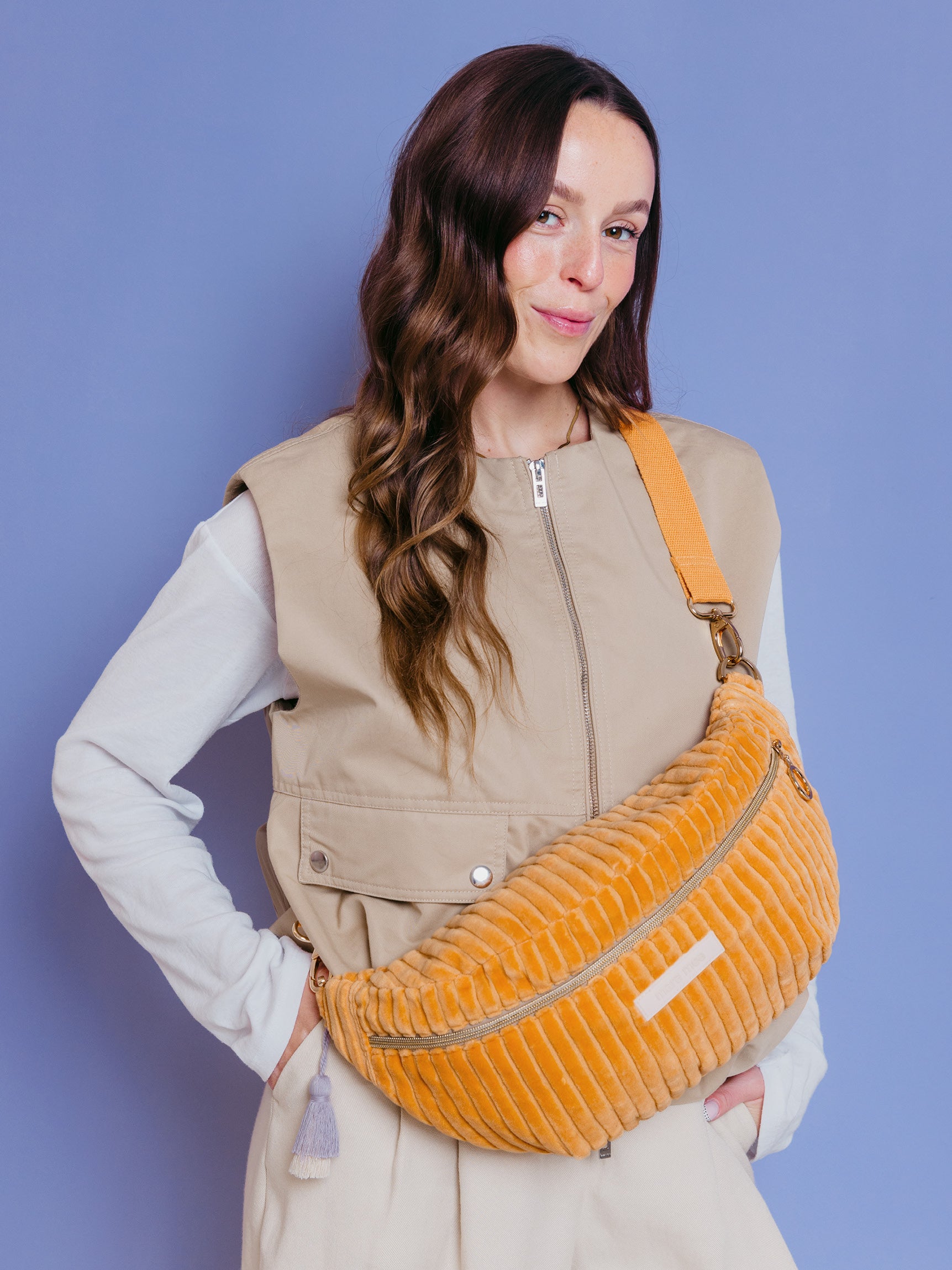 Frau trägt die orangefarbene mara mea Maxi Bauchtasche Soft Serve Peach aus Cord quer über der Brust vor blauem Hintergrund