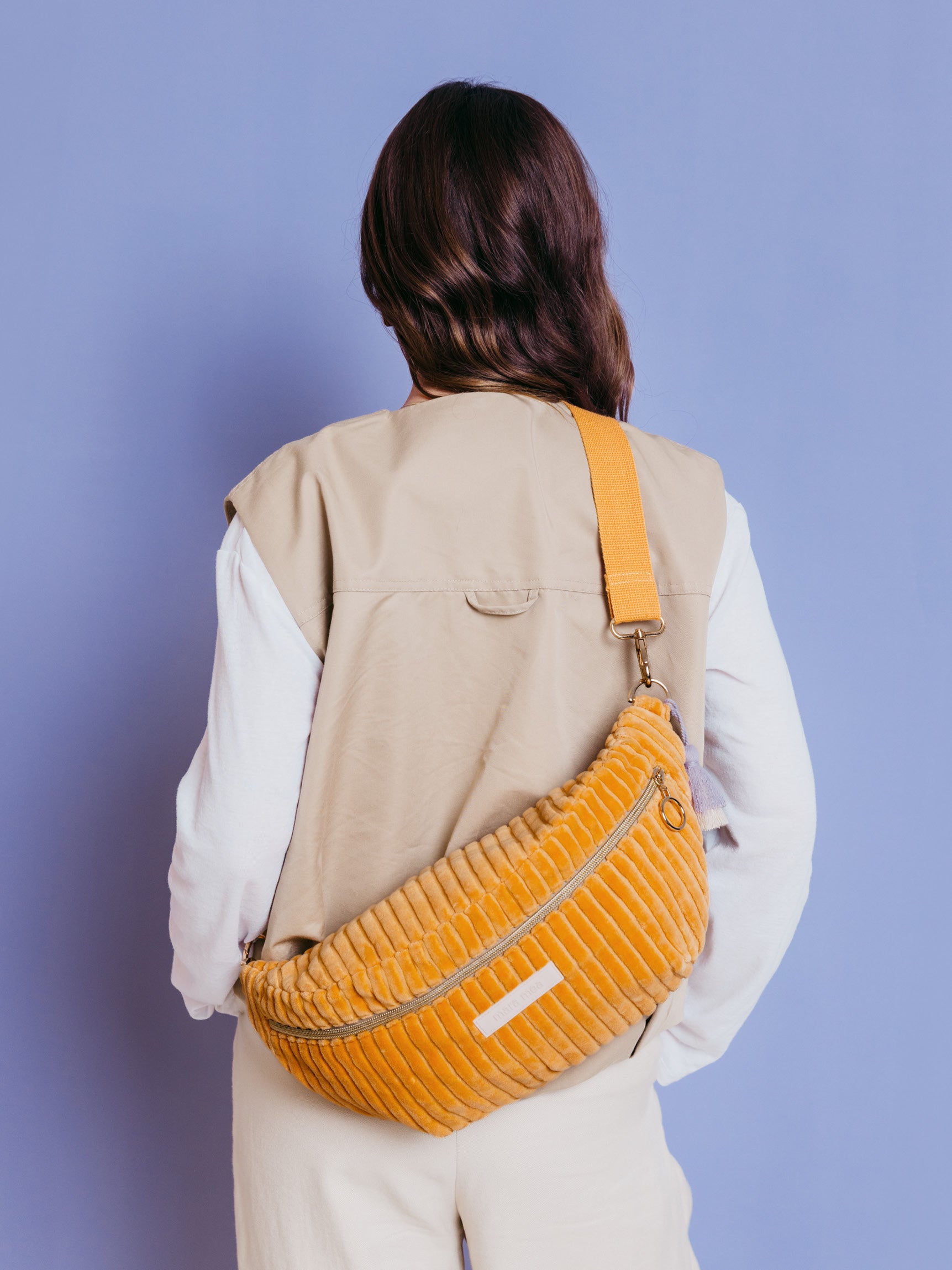 Frau trägt die orangefarbene mara mea Maxi Bauchtasche Soft Serve Peach aus Cord quer über dem Rücken vor blauem Hintergrund