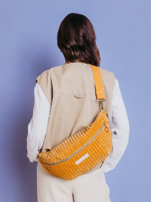 Frau trägt die orangefarbene mara mea Maxi Bauchtasche Soft Serve Peach aus Cord quer über dem Rücken vor blauem Hintergrund