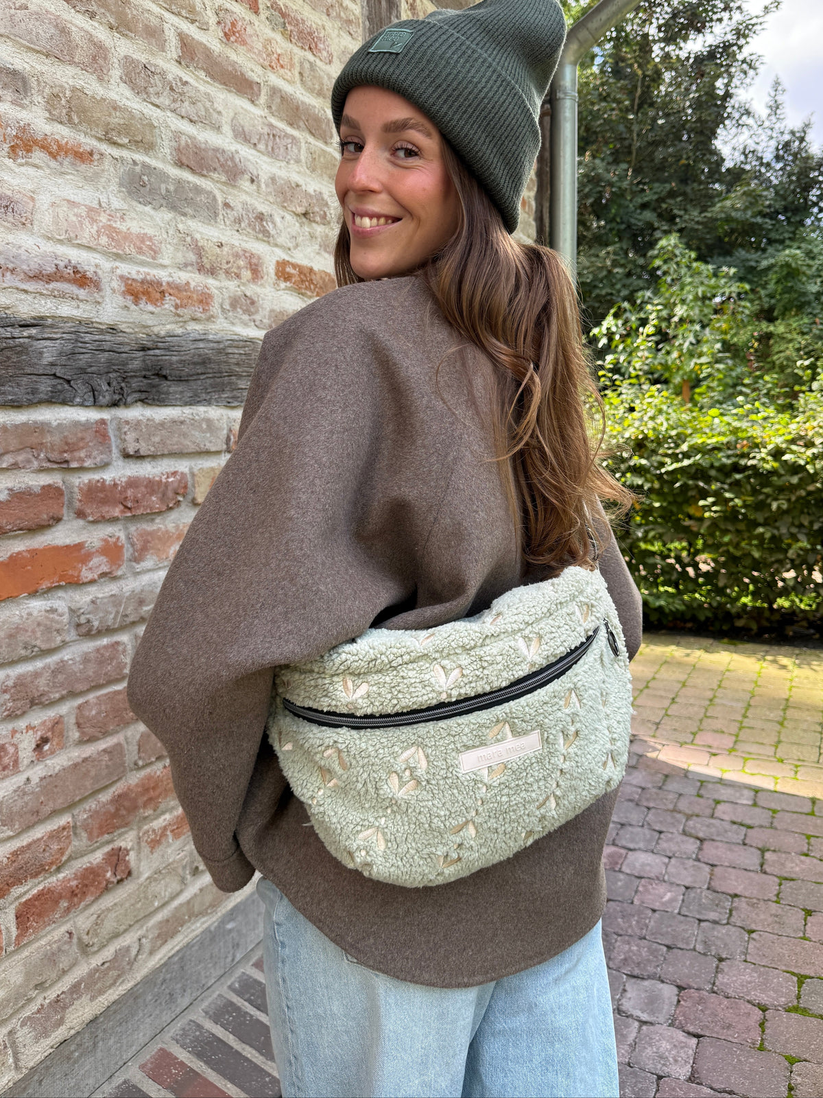 Frau mit grüner Mütze trägt die Maxi Bauchtasche snuggle me auf dem Rücken und lächelt über die Schulter