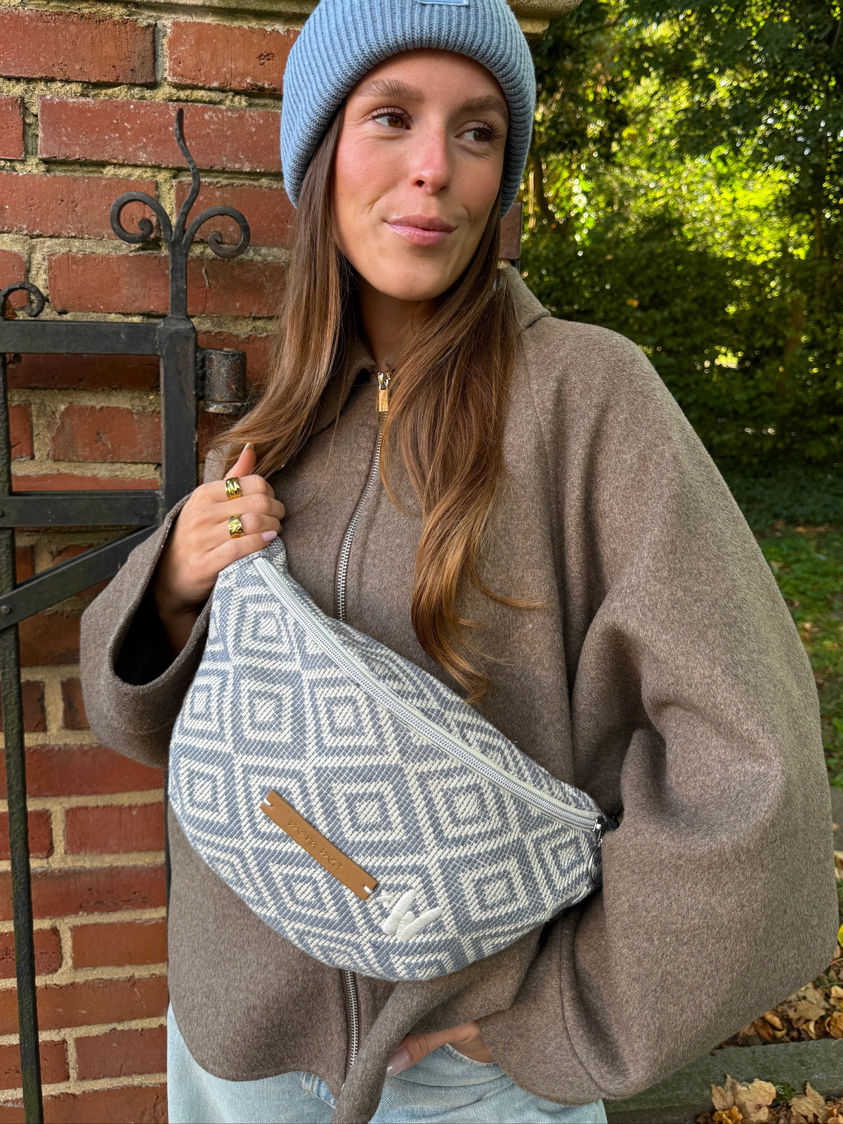 Frau mit blauer Mütze trägt die Midi Bauchtasche vacation ready crossbody vor dem Körper