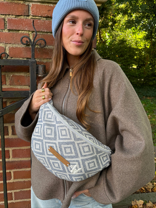 Frau mit blauer Mütze trägt die Midi Bauchtasche vacation ready crossbody vor dem Körper