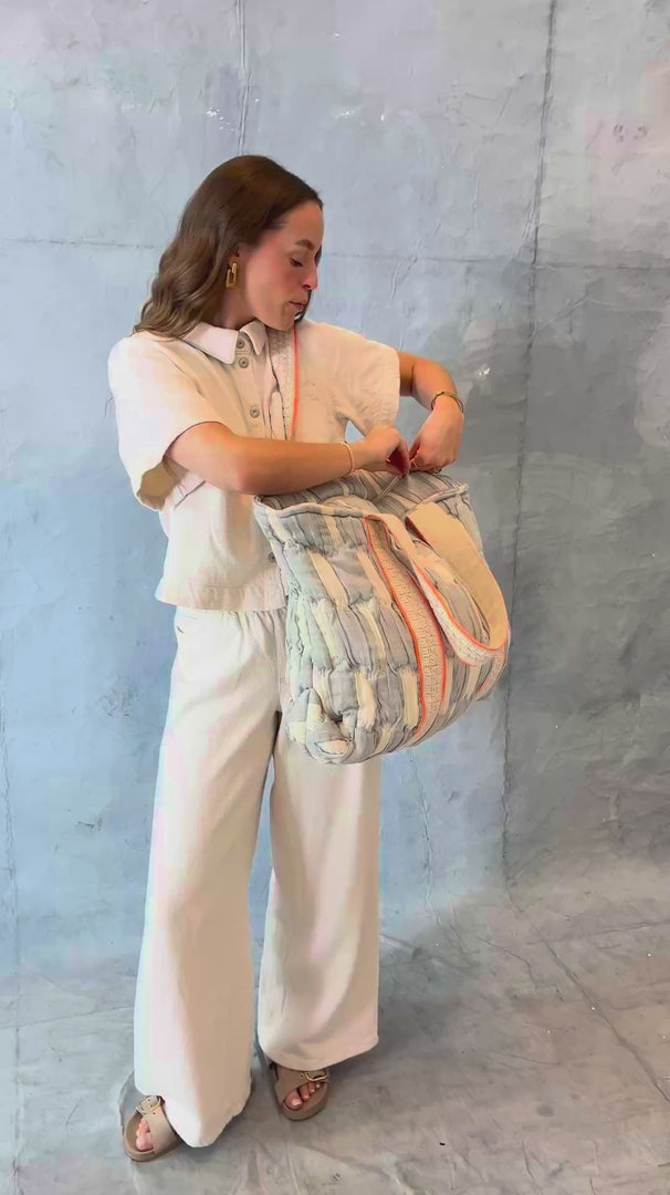 Model öffnet die mara mea Shopper Bag sky state in Hellblau-Offwhite und zeigt Tragegriffe, Reißverschluss und gepolsterten Baumwollstoff