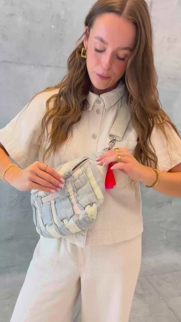 Model öffnet die mara mea Midi Bauchtasche creamy skies in Hellblau-Offwhite und zeigt Reißverschluss, Ring-Zipper und neon-orange-pinke Quaste sowie verschiedenen Tragemöglichkeiten