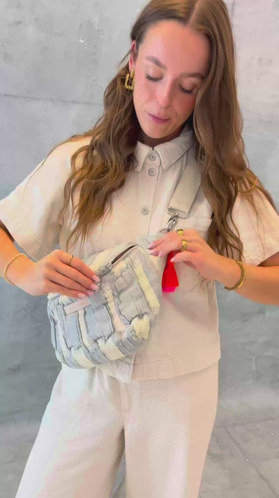 Model öffnet die mara mea Midi Bauchtasche creamy skies in Hellblau-Offwhite und zeigt Reißverschluss, Ring-Zipper und neon-orange-pinke Quaste sowie verschiedenen Tragemöglichkeiten