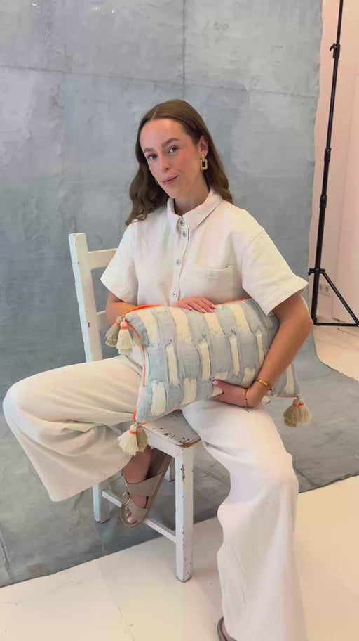 Sitzende Frau präsentiert das mara mea Kissen cotton mood in Hellblau-Beige mit neon-oranger Paspel und Quasten