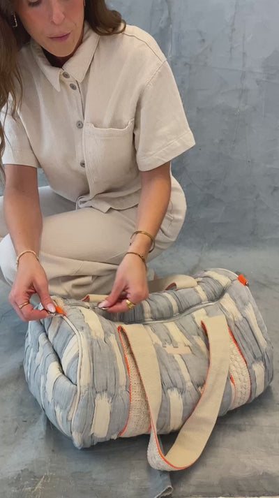 Model öffnet die mara mea Reisetasche breeze babe in Hellblau-Offwhite und zeigt Reißverschluss, Tragegriffe und neon-orange Details