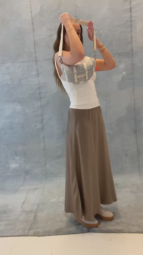Model legt die mara mea Mini Bauchtasche cloud club in Hellblau-Offwhite mit verstellbarem Gurt und neon-orange-pinker Quaste an und zeigt Tragevarianten
