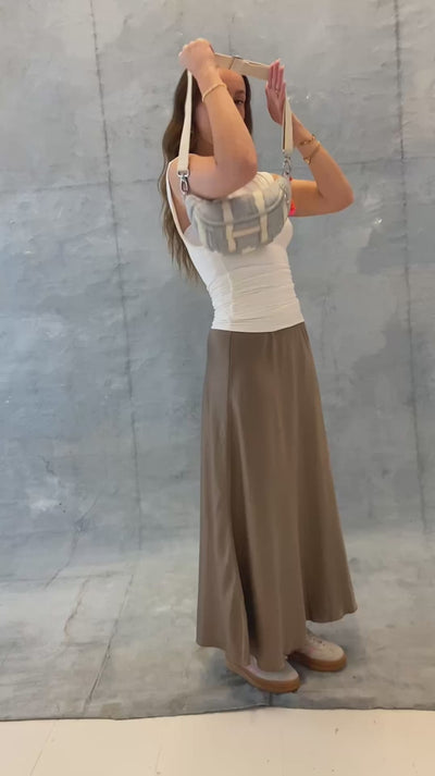 Model legt die mara mea Mini Bauchtasche cloud club in Hellblau-Offwhite mit verstellbarem Gurt und neon-orange-pinker Quaste an und zeigt Tragevarianten
