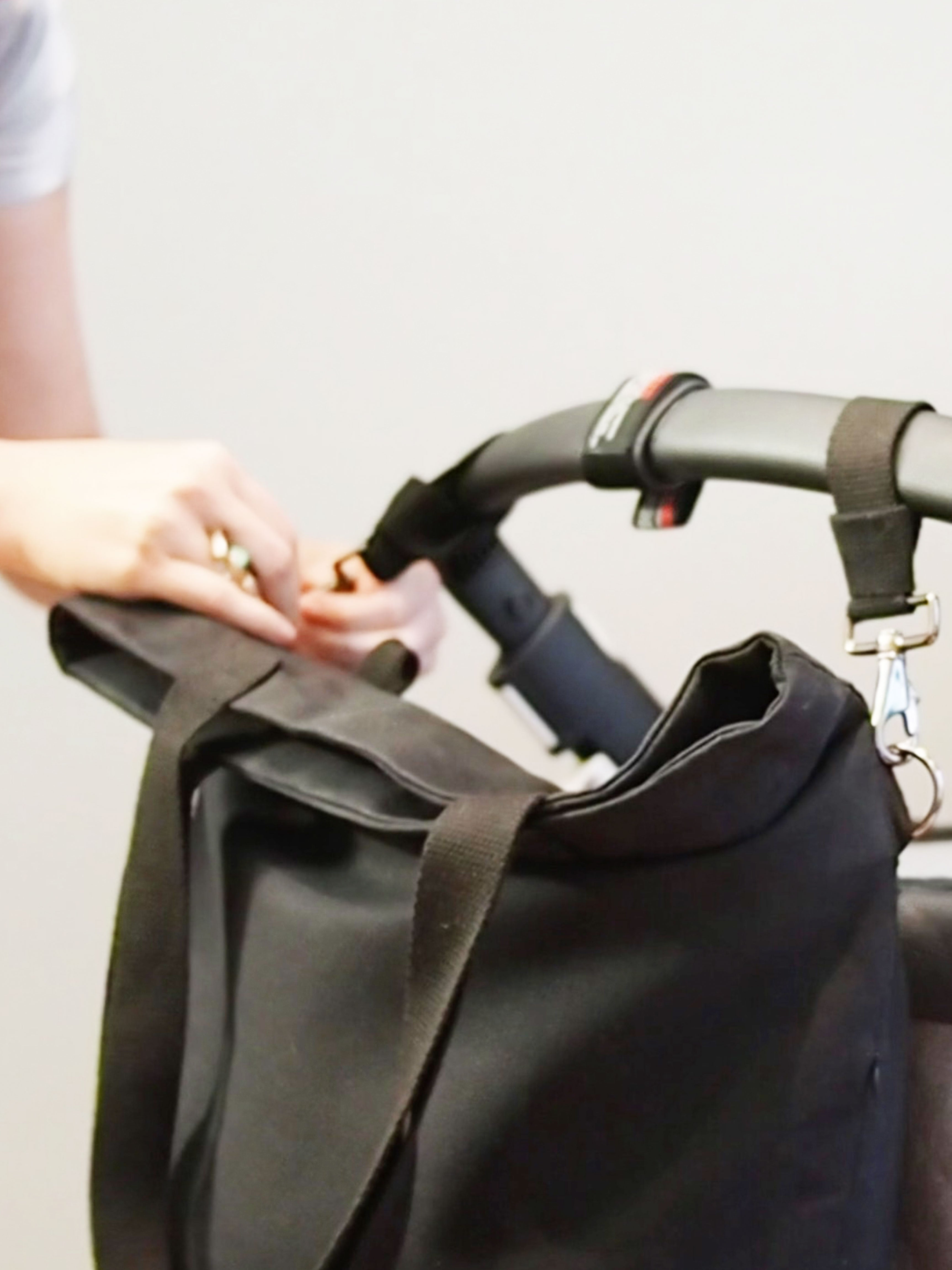 Durch die dunkelblauen Kinderwagenhalterungen von mara mea kann man die Handtasche am Kinderwagen befestigen.