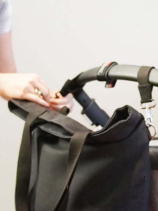 Durch die dunkelblauen Kinderwagenhalterungen von mara mea kann man die Handtasche am Kinderwagen befestigen.