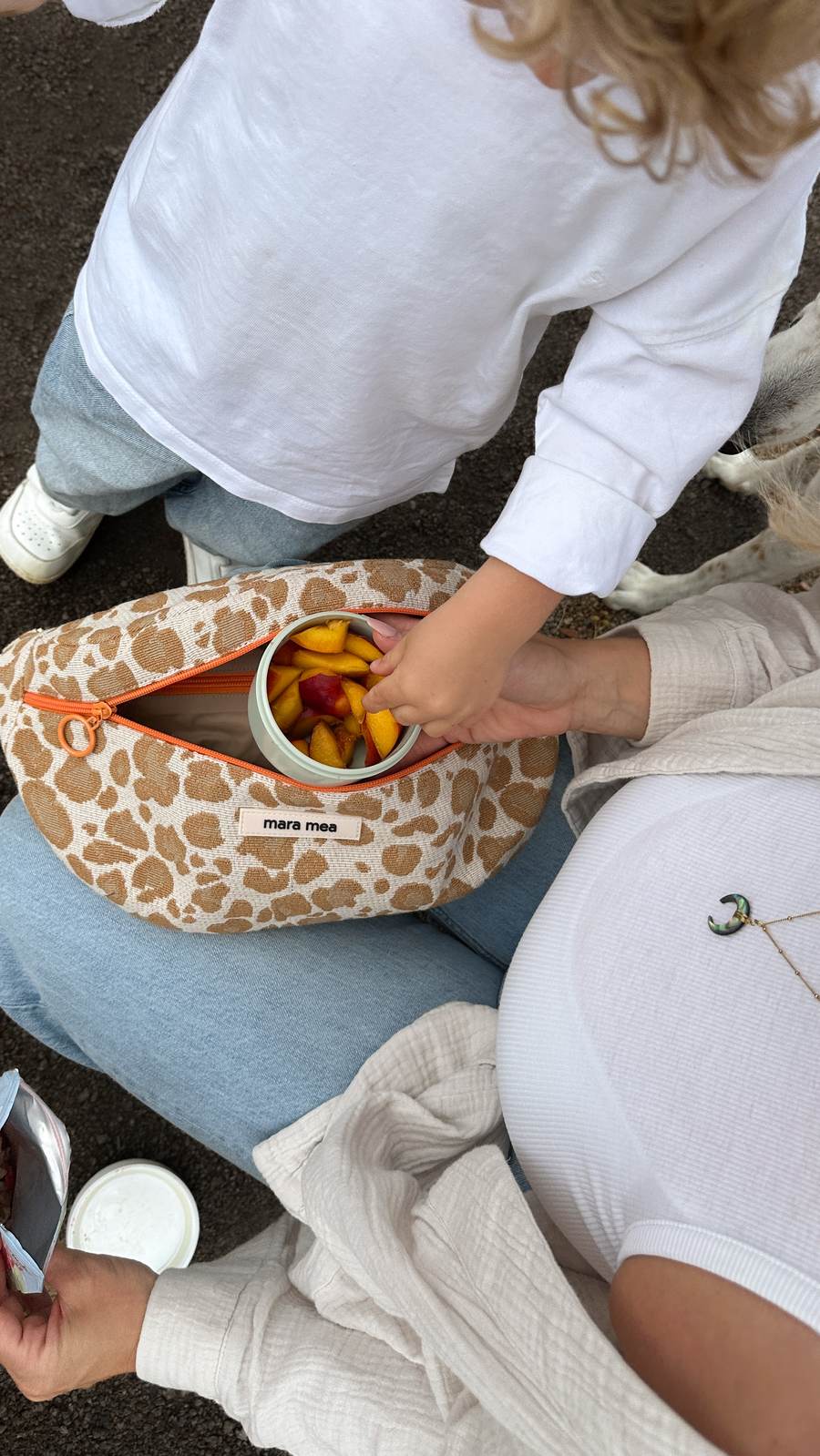 Geöffnete mara mea Tasche mit Snackbox – eine Kinderhand greift nach Obst